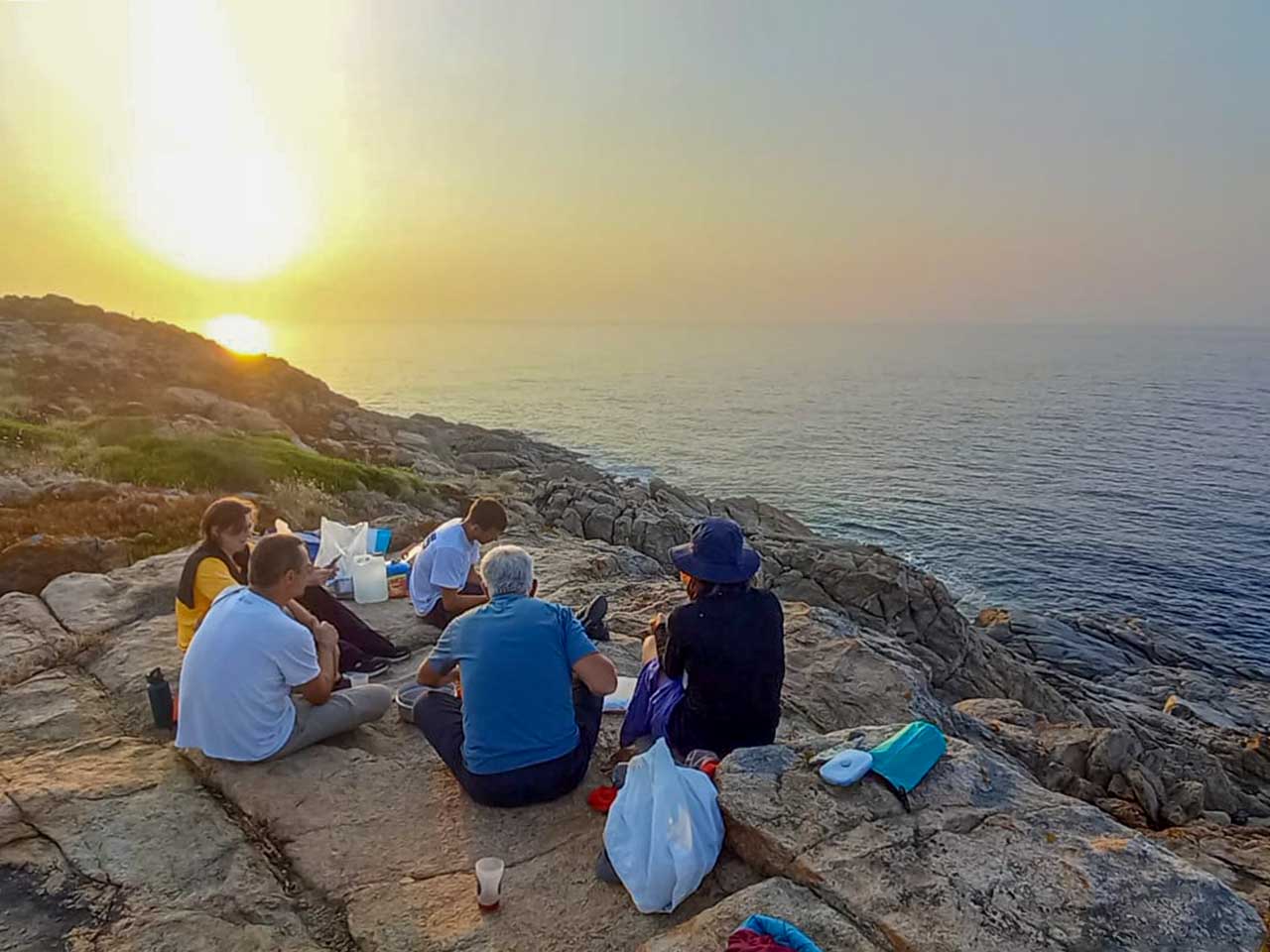 Groupe de personnes sur des rochers admirant le coucher de soleil sur le mer